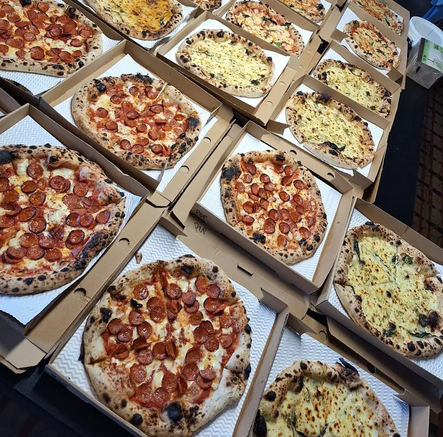 A dozen open pizza boxes laid out side by side, pepperoni and garlic bread pizzas ready to go out.