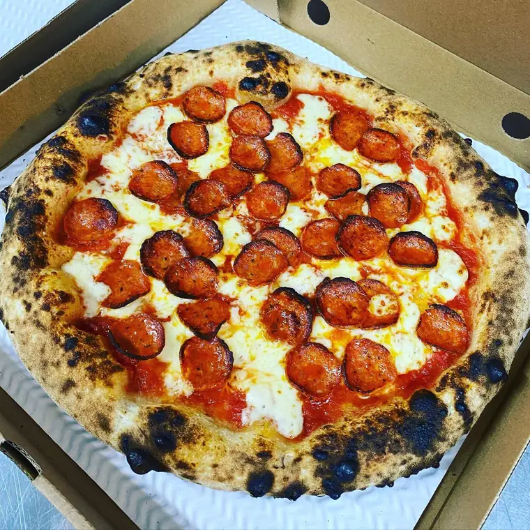 A double-pepperoni pizza in an open box, its Neapolitan crust puffed and charred in patches.